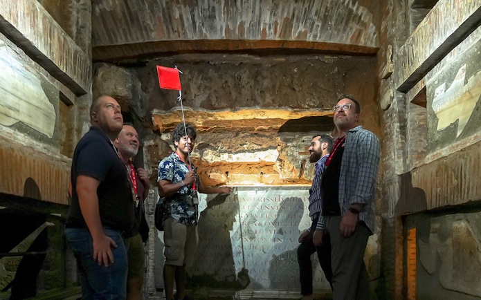 Visitors with guide inside Capuchin Crypt, Rome, observing ancient inscriptions.