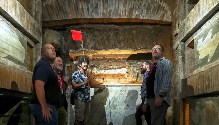 Visitors with guide inside Capuchin Crypt, Rome, observing ancient inscriptions.