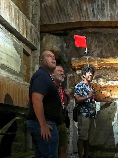 Visitors with guide inside Capuchin Crypt, Rome, observing ancient inscriptions.
