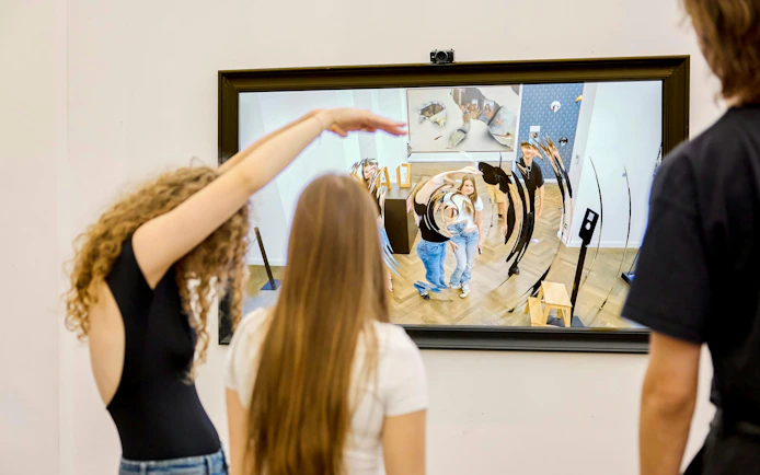Visitors interacting with a distorted mirror at IAM Illusion Art Museum, Prague.