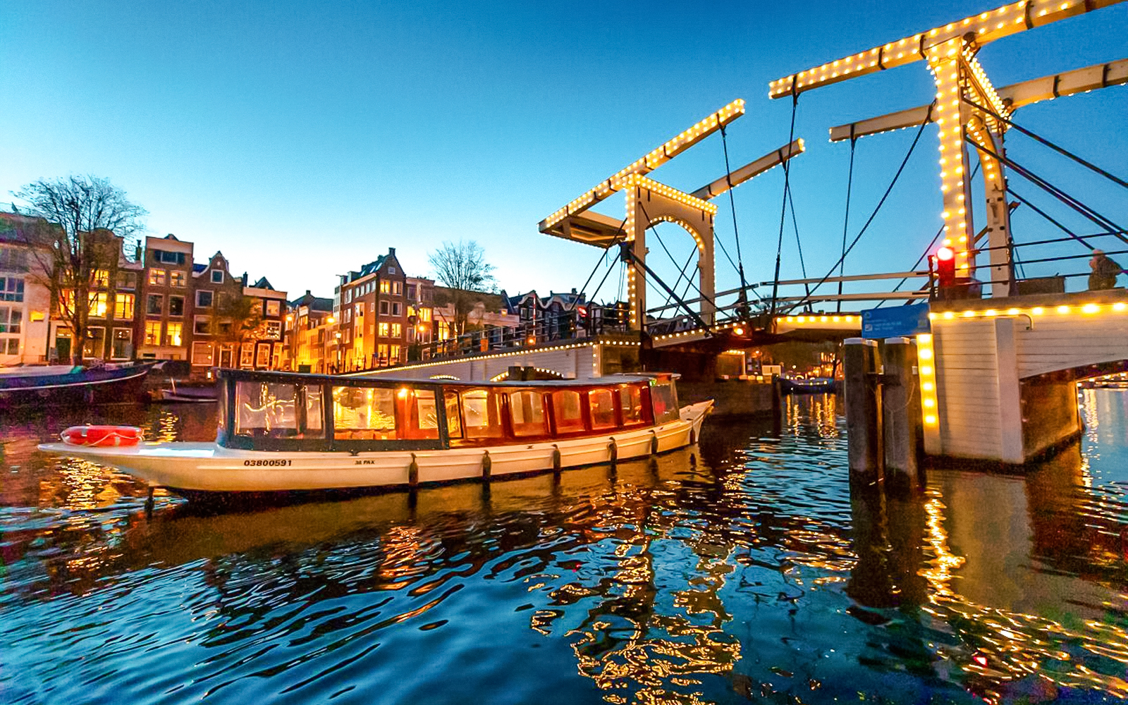 Canal boat cruising under illuminated bridge during Amsterdam Light Festival.
