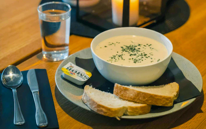 Creamy soup with chives, bread slices, and butter on a plate, Sommarøy Fjord Day, Tromsø.