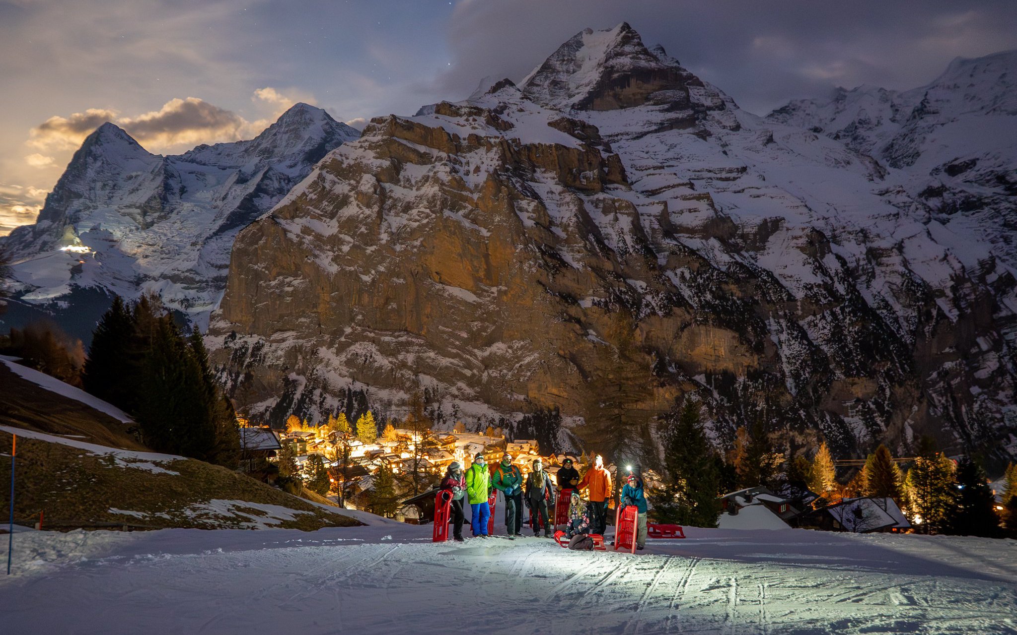 Group sledding at night with illuminated mountains in Interlaken, Switzerland.