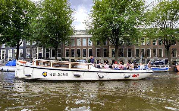 Guests enjoying Amsterdam smoke-friendly canal cruise on a boat with city buildings in the background.