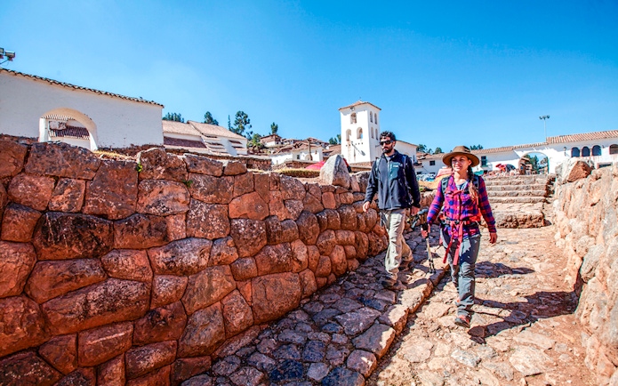 Tourists walking along stone pathways in Chinchero, Peru, with traditional architecture in the background.
