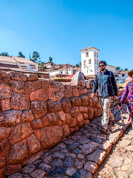 Tourists walking along stone pathways in Chinchero, Peru, with traditional architecture in the background.