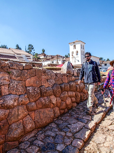 Tourists walking along stone pathways in Chinchero, Peru, with traditional architecture in the background.