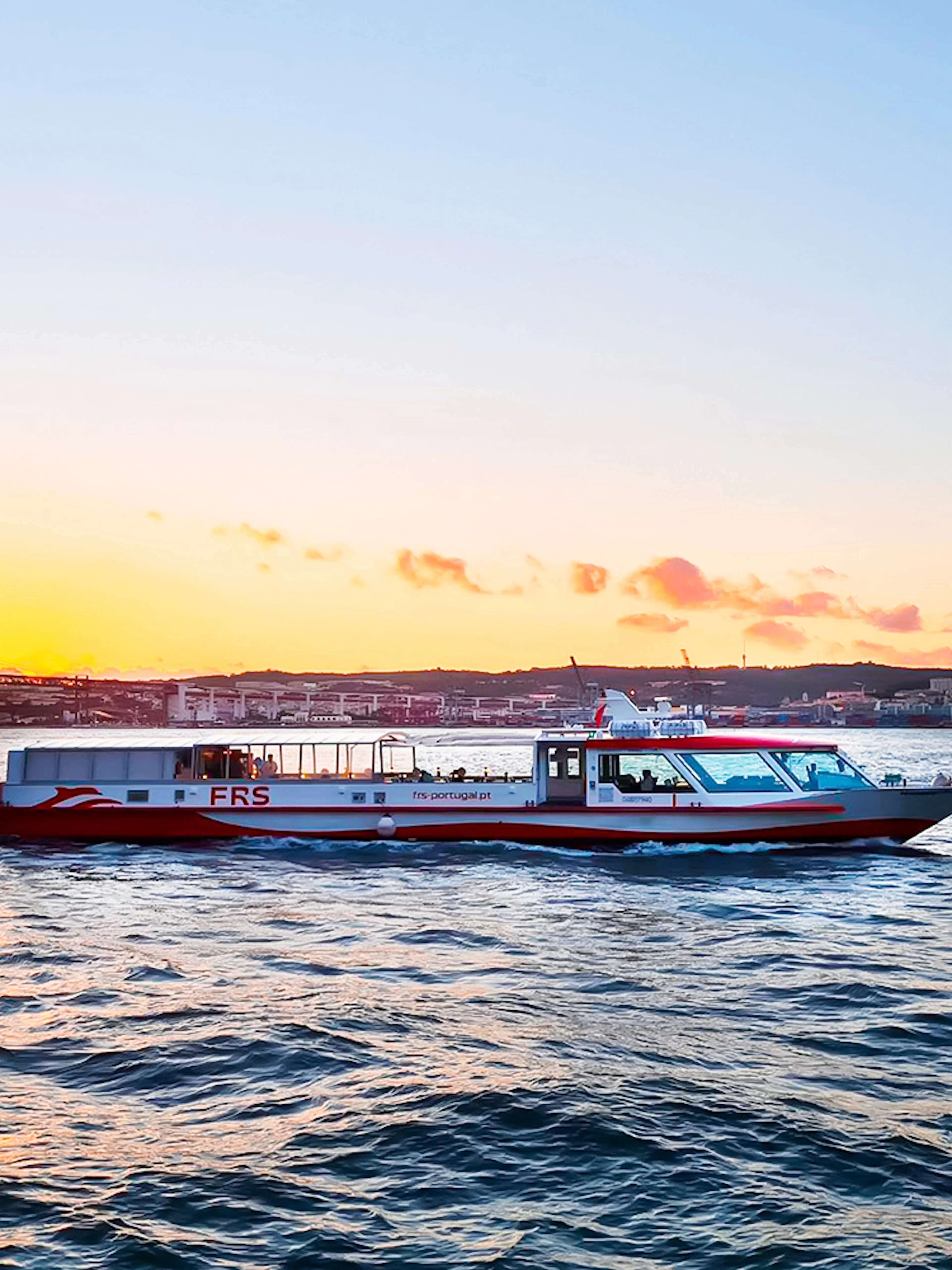 Cruise boat on Tagus River at sunset with Lisbon's skyline in the background.