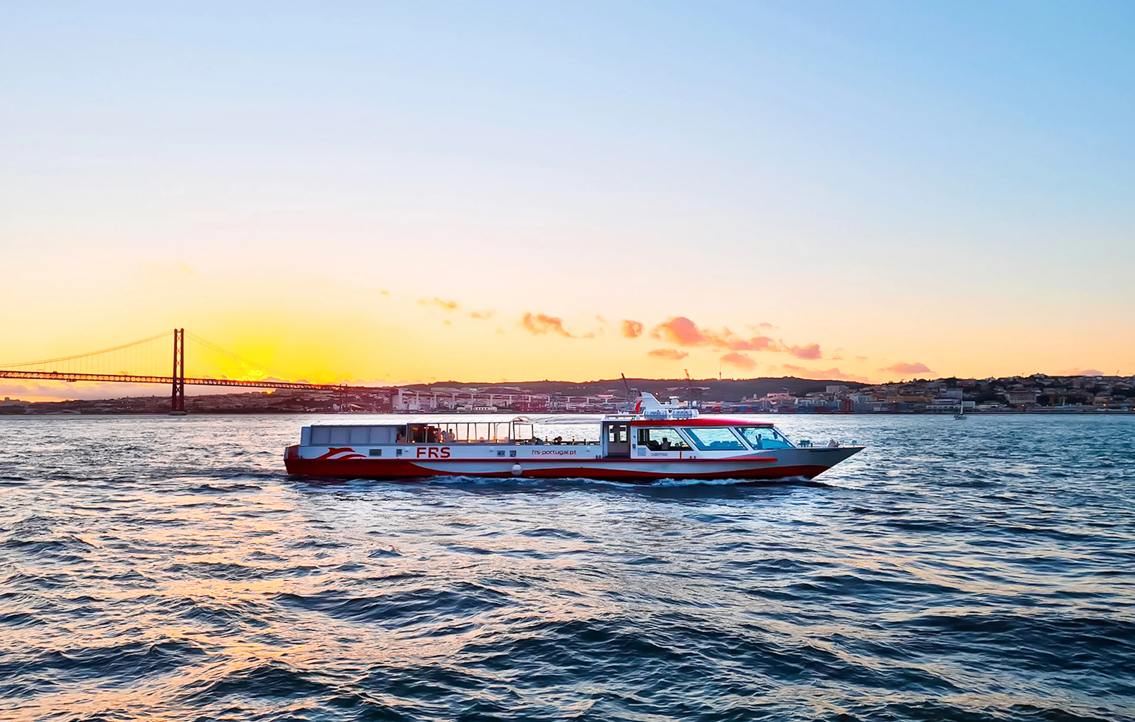 Cruise boat on Tagus River at sunset with Lisbon's skyline in the background.