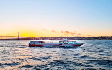 Cruise boat on Tagus River at sunset with Lisbon's skyline in the background.
