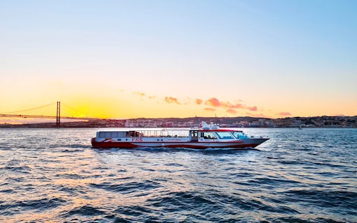 Cruise boat on Tagus River at sunset with Lisbon's skyline in the background.