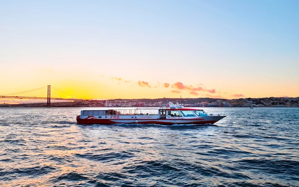 Cruise boat on Tagus River at sunset with Lisbon's skyline in the background.