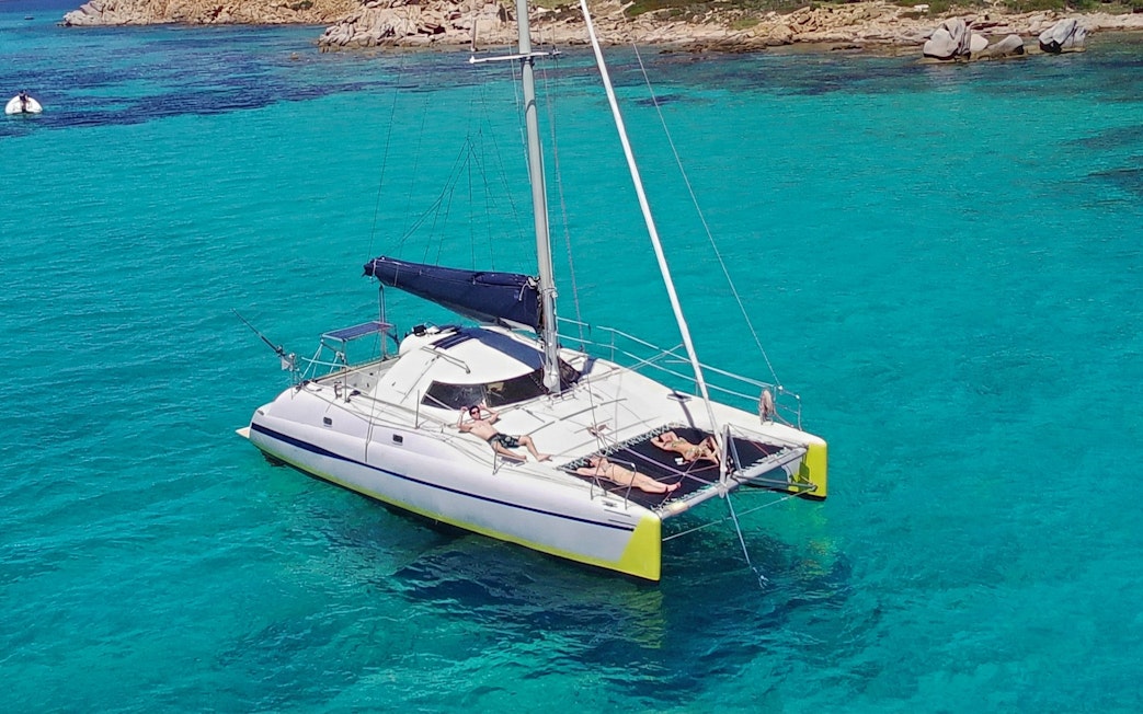 Catamaran sailing near Tavolara Island with people relaxing on deck.
