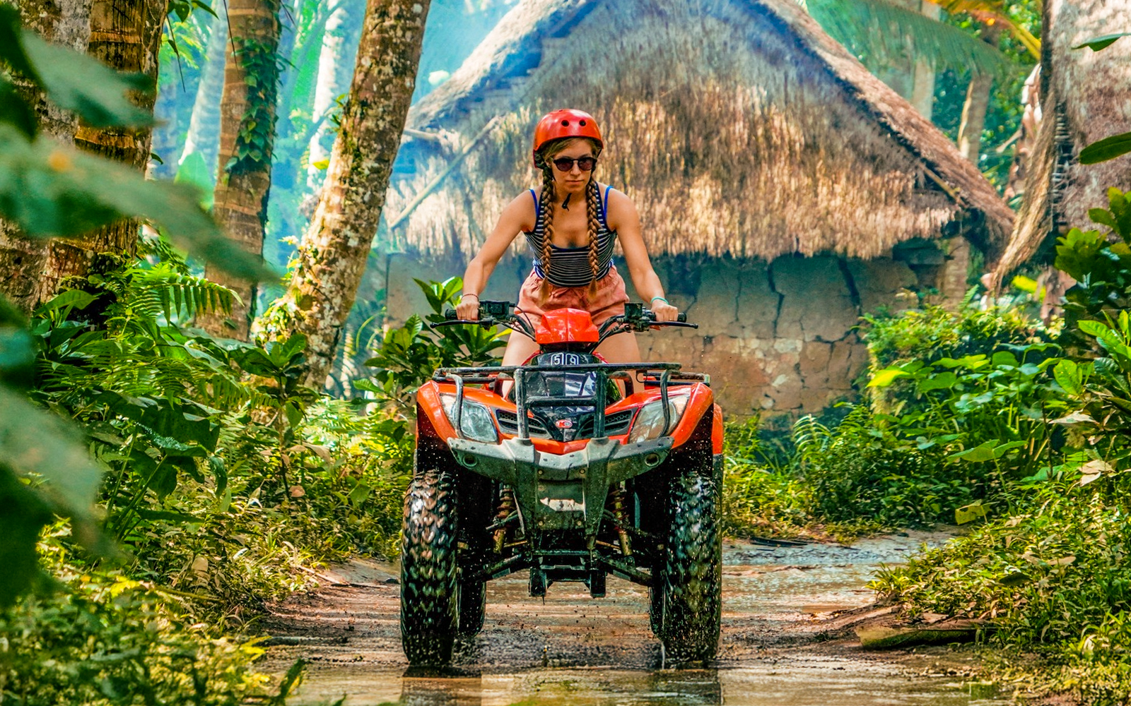 ATV rider navigating jungle path in Ubud with traditional huts in background.