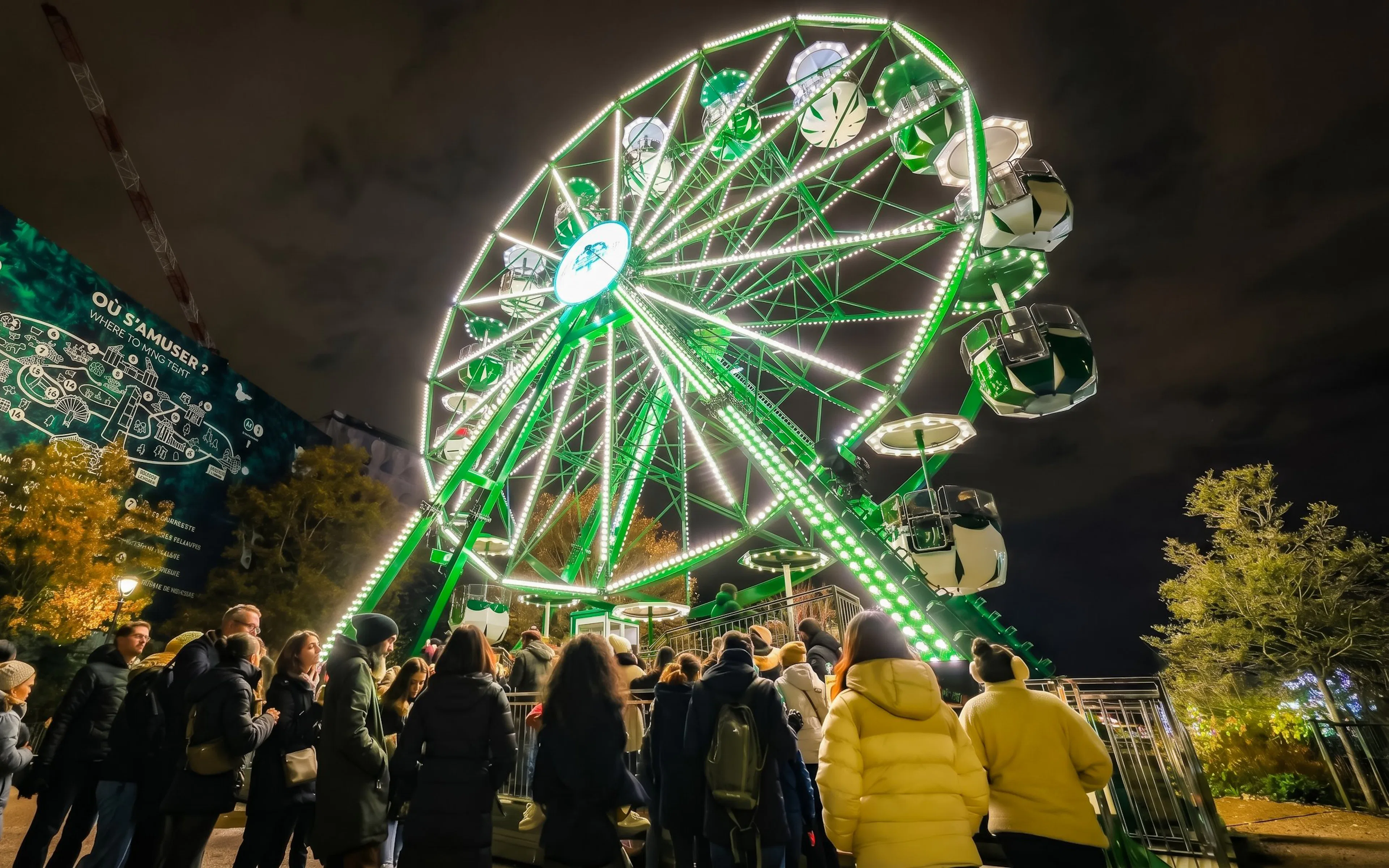 Ferris wheel illuminated at night with people in line at Jardin d'acclimatation, Paris.