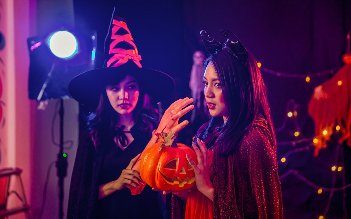 Two people in Halloween costumes holding a carved pumpkin during Bran Dracula's Castle tour.