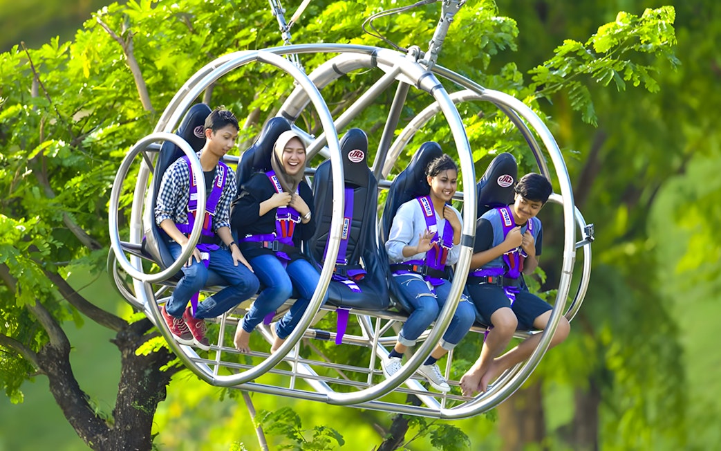 People enjoying the Slingshot ride in Singapore amidst lush greenery.