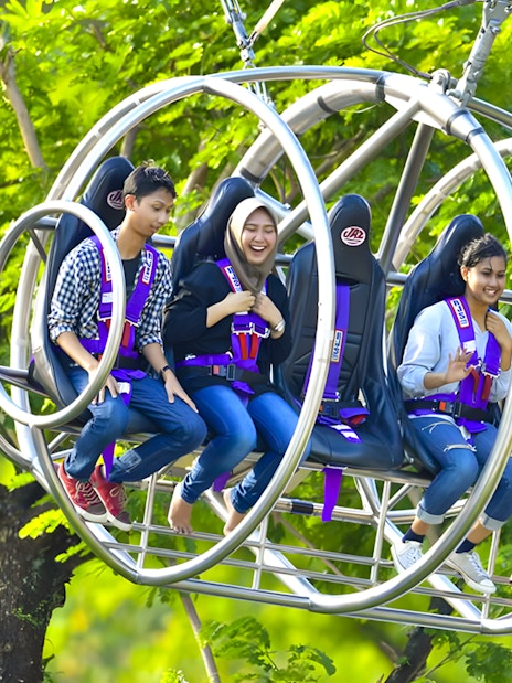 People enjoying the Slingshot ride in Singapore amidst lush greenery.