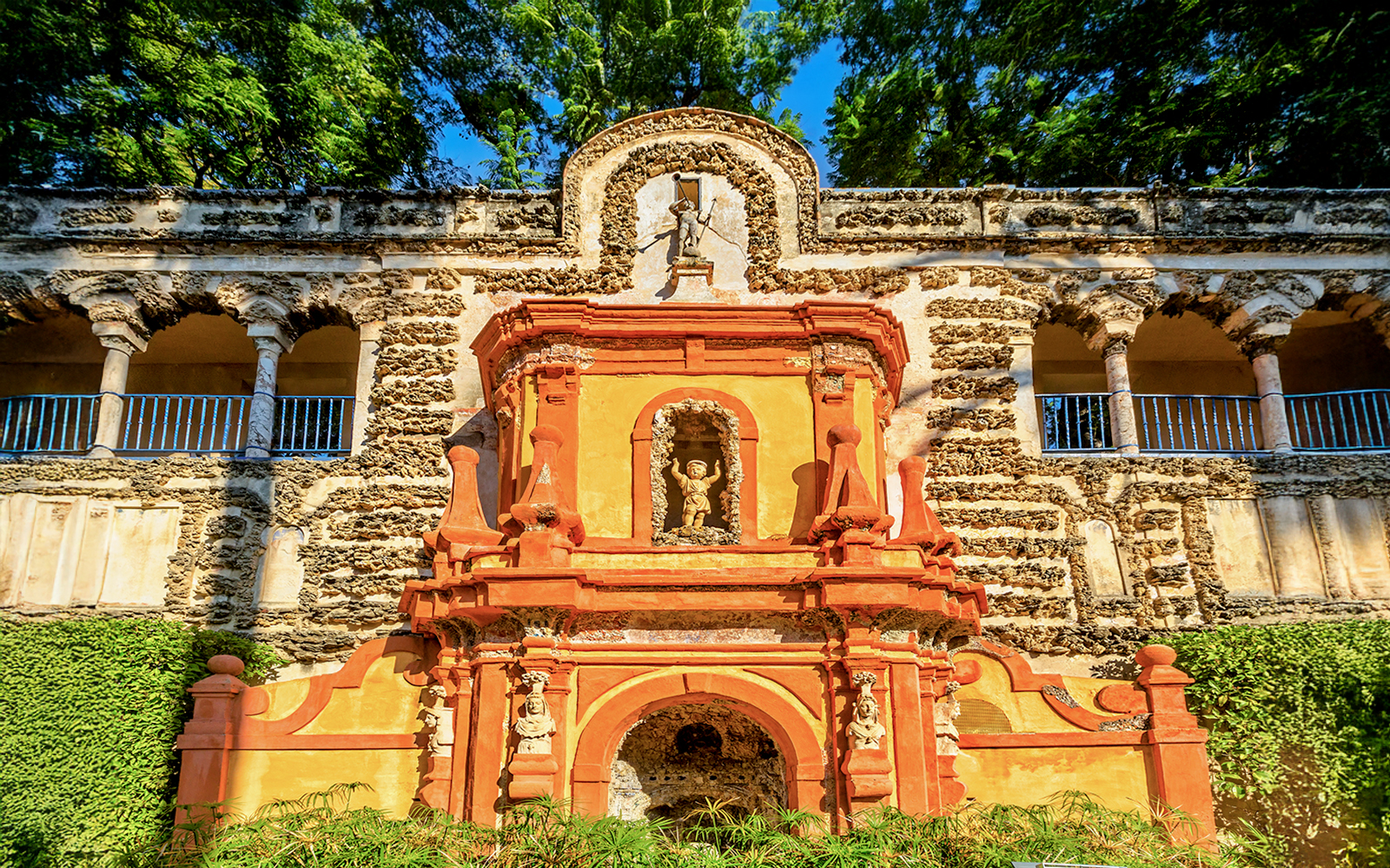Fountain of Fame in Royal Alcazar, Seville, Spain, with intricate stone carvings and lush garden backdrop.
