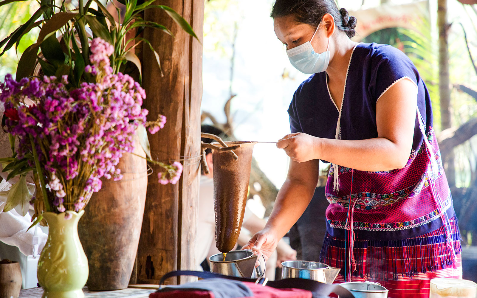 Woman in traditional attire brewing coffee on Doi Inthanon tour.