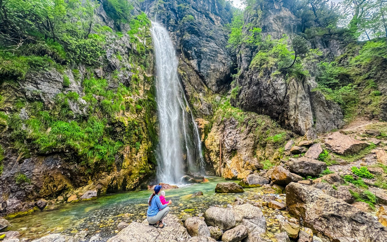 Person sitting near Grunas waterfall in Albania, surrounded by rocky cliffs and greenery.
