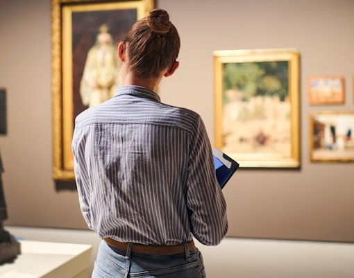 Backshot of a woman standing in front of a painting in the musuem