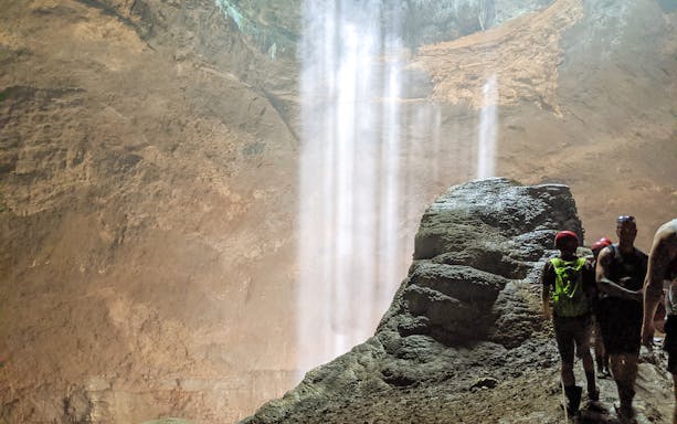 Visitors exploring a cave with a waterfall on a tailor-made private day tour.