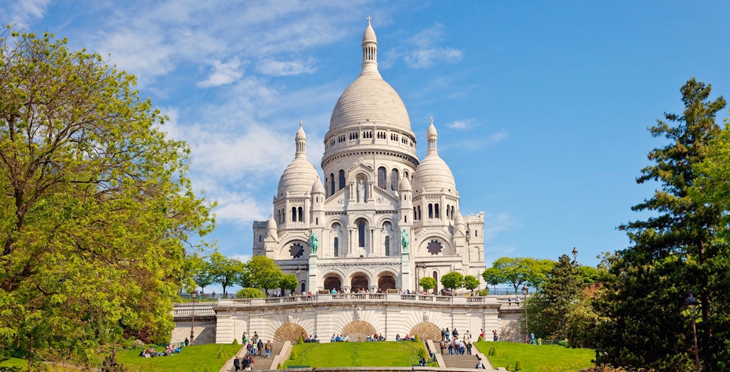 Basilica of the Sacred Heart of Paris with tourists on steps, Paris cityscape in background.