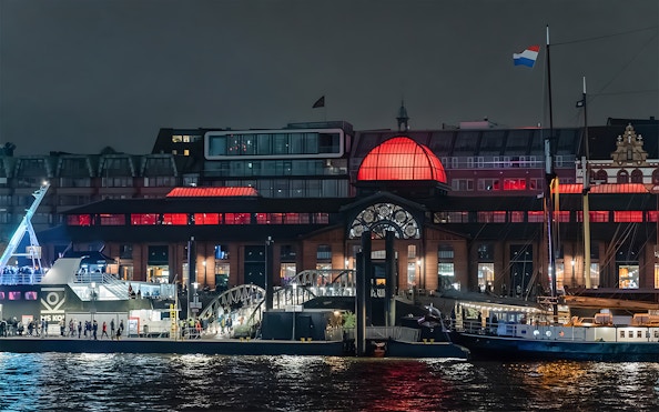Grand Harbor evening cruise with illuminated waterfront building and docked ship.