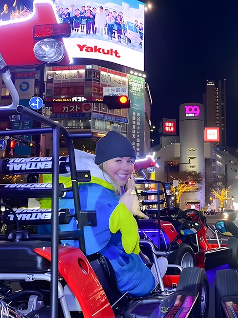 People in go-karts posing in Shibuya at night with bright city lights and billboards.