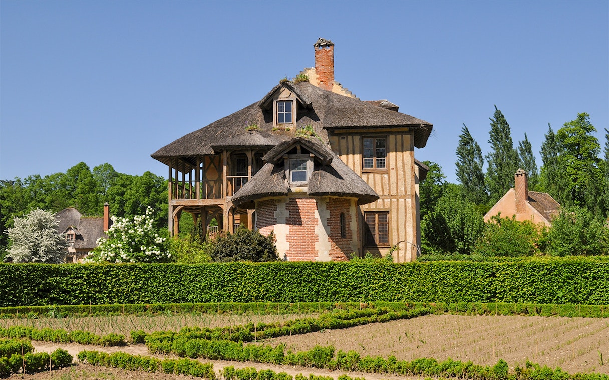 Thatched cottage in Queen's Hamlet, Versailles, surrounded by gardens and greenery.