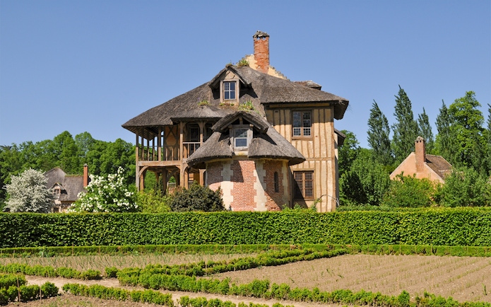 Thatched cottage in Queen's Hamlet, Versailles, surrounded by gardens and greenery.