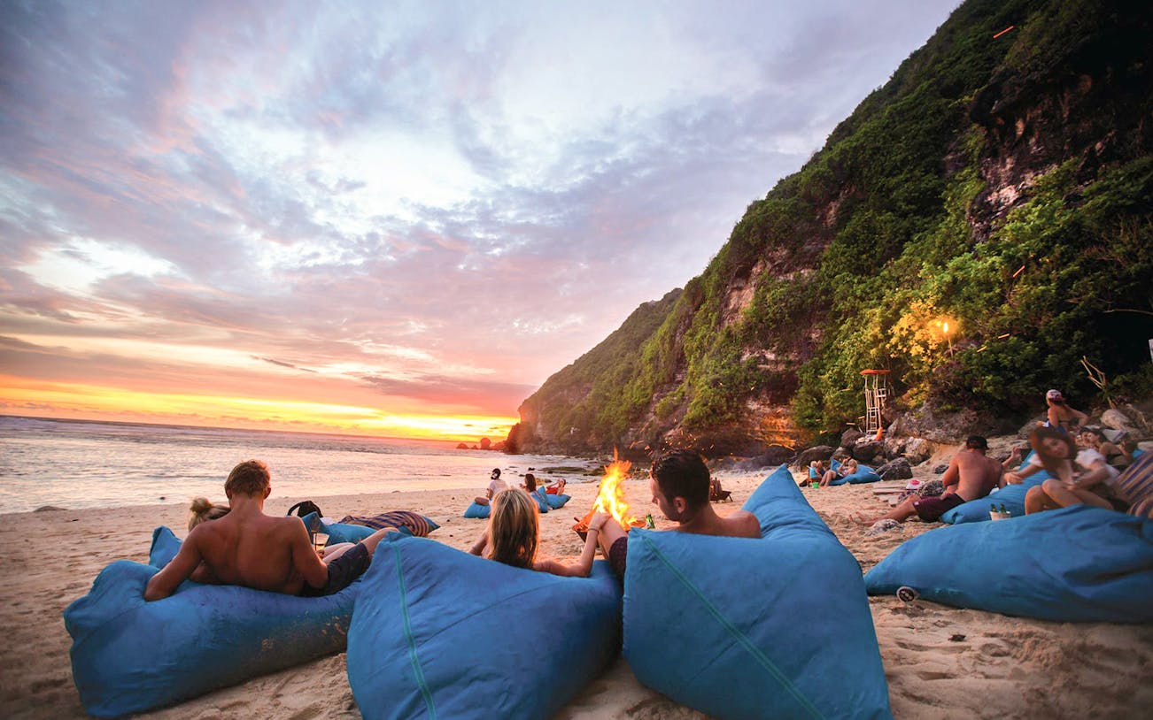 Beachgoers relaxing on bean bags at sunset, Finns Beach Club Bali.
