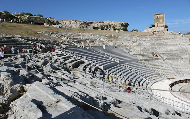Greek Theater of Syracuse with visitors exploring ancient stone seating.