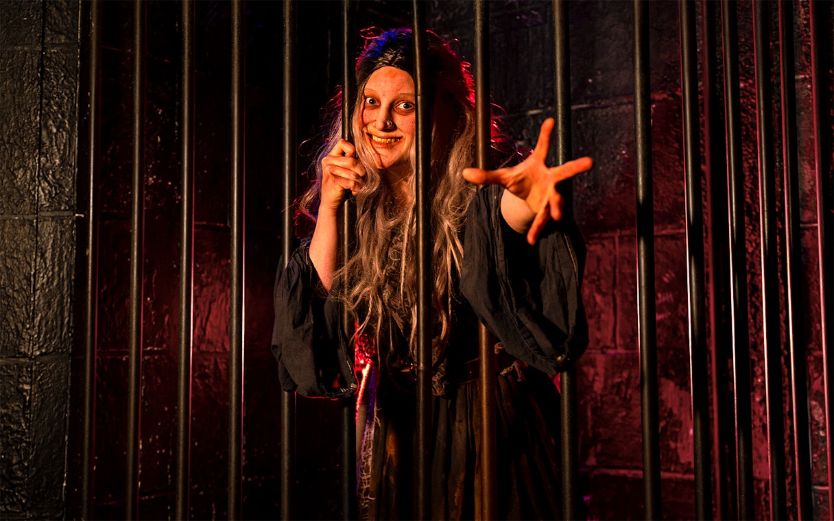 Witch role-playing behind bars at London Dungeon.