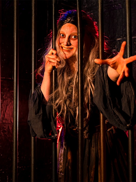 Witch role-playing behind bars at London Dungeon.