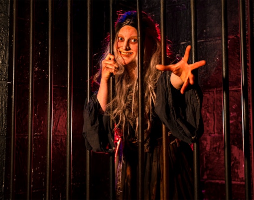 Witch role-playing behind bars at London Dungeon.