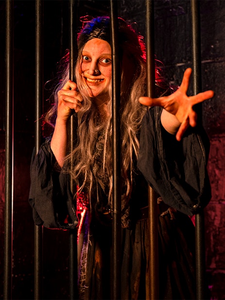 Witch role-playing behind bars at London Dungeon.