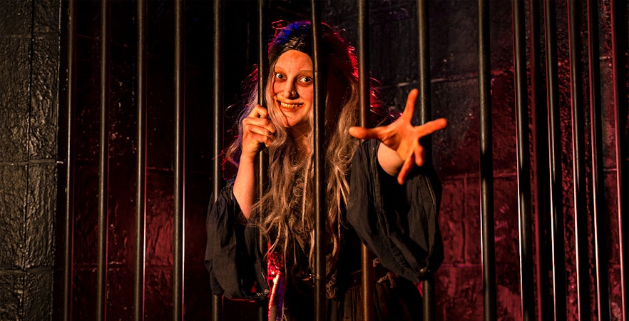 Witch role-playing behind bars at London Dungeon.