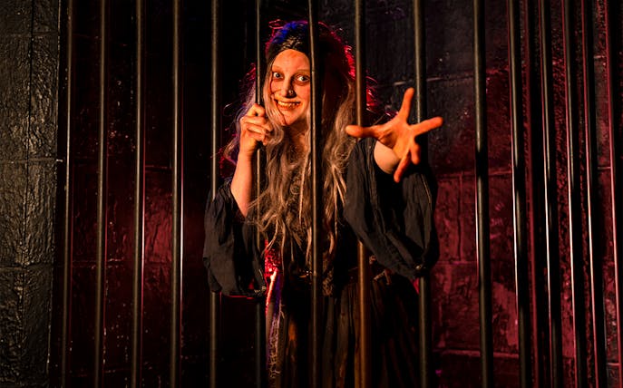 Witch role-playing behind bars at London Dungeon.