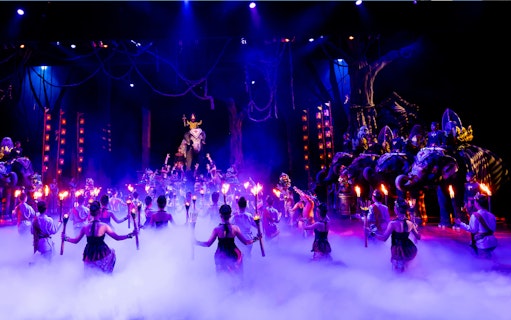 Performers with torches in a vibrant Phuket Fantasea show featuring elephants on stage.