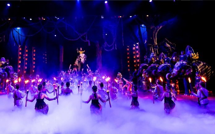 Performers with torches in a vibrant Phuket Fantasea show featuring elephants on stage.