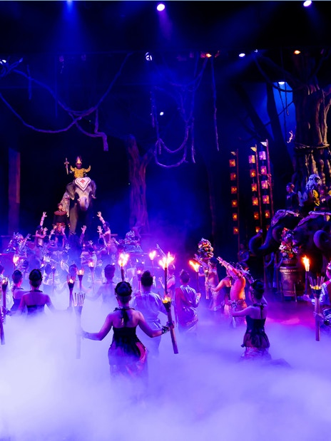 Performers with torches in a vibrant Phuket Fantasea show featuring elephants on stage.