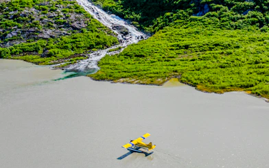 Seaplane landing on a lake near a lush green hillside with a waterfall, Norris Adventure.