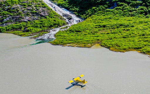 Seaplane landing on a lake near a lush green hillside with a waterfall, Norris Adventure.
