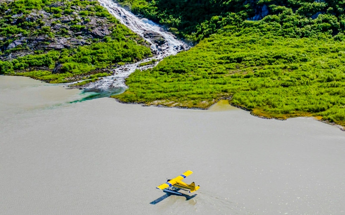 Seaplane landing on a lake near a lush green hillside with a waterfall, Norris Adventure.