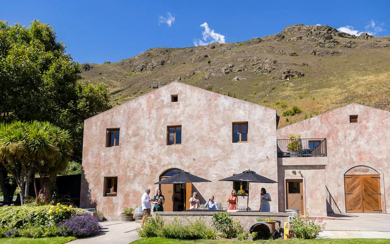 Winery visitors enjoying a tasting outside a rustic building in Queenstown.
