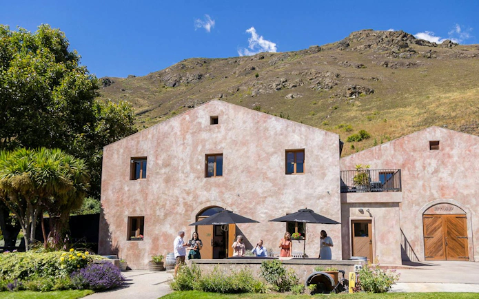 Winery visitors enjoying a tasting outside a rustic building in Queenstown.