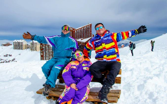 Tourists in colorful ski gear at Valle Nevado with snowy mountains and buildings in the background.