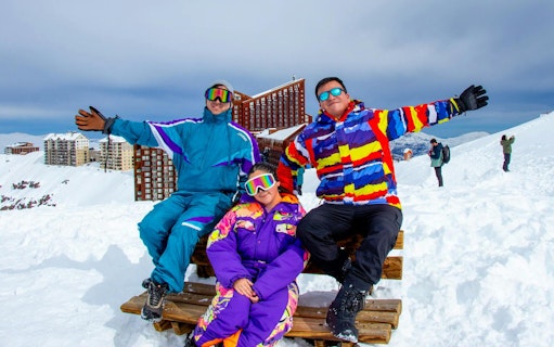 Tourists in colorful ski gear at Valle Nevado with snowy mountains and buildings in the background.